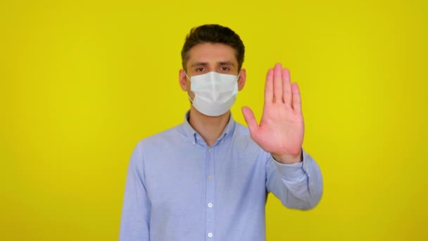 Young man in a medical mask looks at camera and holds out hand in front — Stock video