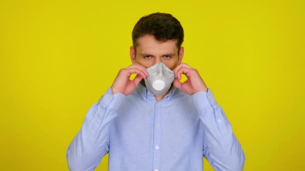 Young man puts on a protective mask on yellow background — Stock videók