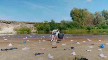 Man collects plastic trash on banks of polluted river and shows thumbs up