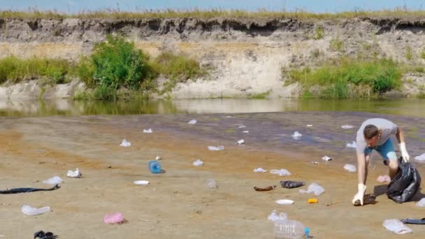 Man is dancing, singing acollects plastic trash on banks of polluted river — Stock video