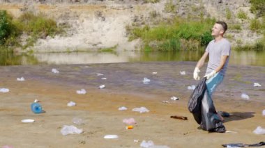 Adam kirlenmiş nehir kıyısında plastik çöp topluyor ve en sevdiği şarkıyı dinliyor.