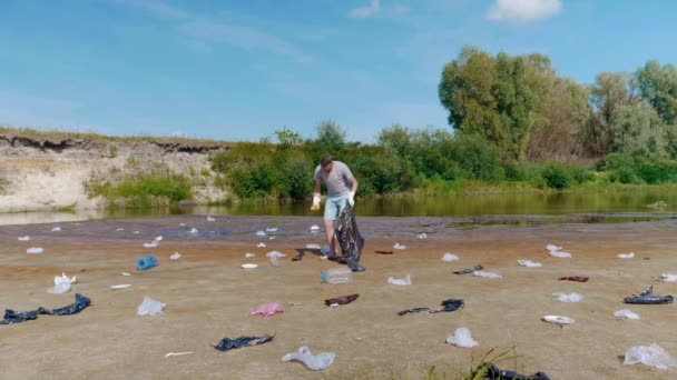 Homem é coleta lixo de plástico nas margens do rio poluído e mostra polegares para cima — Vídeo de Stock