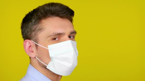 Hombre con máscara médica se pone de perfil y gira la cabeza a la cámara — Vídeos de Stock