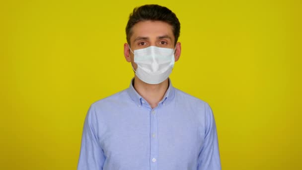 Ung man i en medicinsk mask tittar på kameran på gul bakgrund — Stockvideo