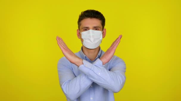 Young man in a medical mask looks at camera and keeps his arms crossed — Αρχείο Βίντεο