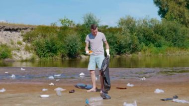 Man collects plastic trash on banks of polluted river and shows thumbs up