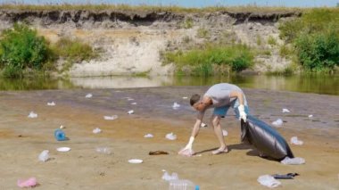 Adam kurumuş ve kirlenmiş bir nehrin kıyısında plastik çöp topluyor.