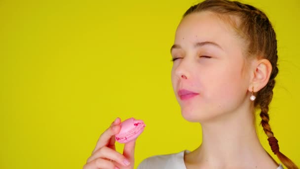 Tiener meisje in een wit T-shirt bijt een roze macaroon en geniet van zijn smaak — Stockvideo