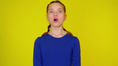 Teenage girl in blue pullover is surprised, opens her mouth and looks at camera.