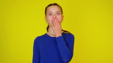 Teenage girl in blue pullover is covers her mouth with hand and very surprised.