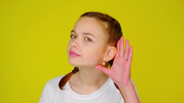 Teenage girl in a white T-shirt puts a palm to her ear, does not hear, listens. — Stock video