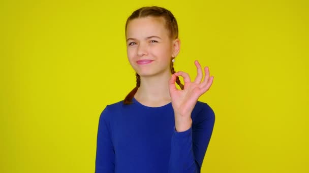 Tonårstjej i blå pullover visar ok på gul bakgrund — Stockvideo