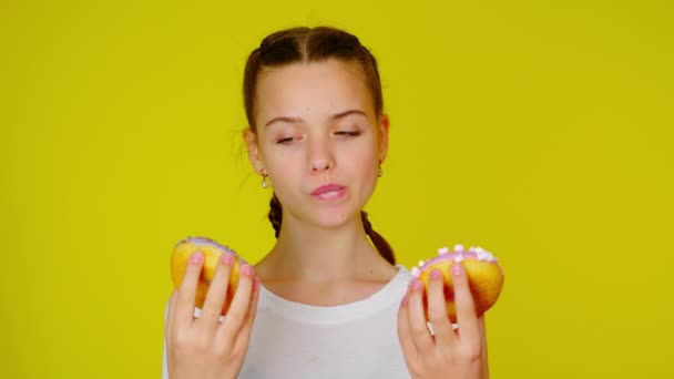 Tiener meisje in een wit T-shirt kijkt naar donuts en wil ze eten. — Stockvideo