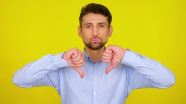 Young man in light blue shirt shows dislike, thumb down.