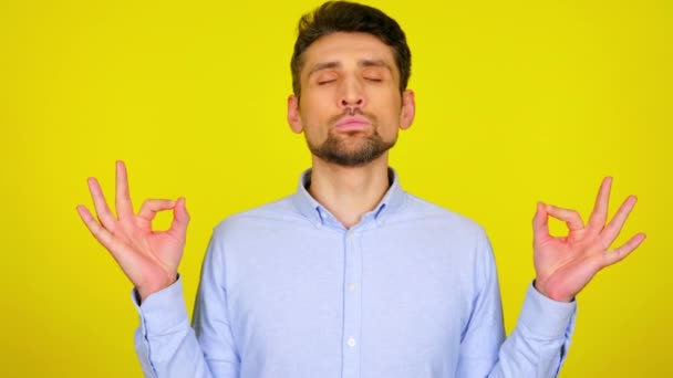 Hombre joven en camisa azul claro está meditando sobre fondo amarillo — Vídeos de Stock
