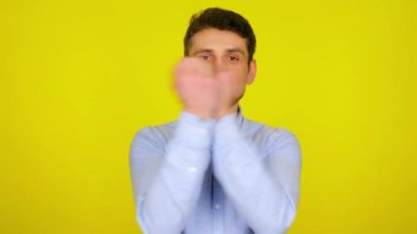 Young man in light blue shirt is wavin his hands and smiles.
