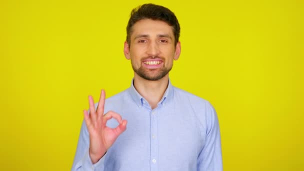 Jongeman in lichtblauw shirt lacht en toont OK. — Stockvideo