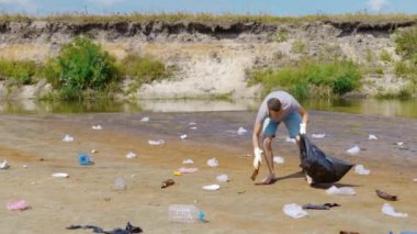 Kızgın adam kirlenmiş nehrin kıyısında plastik çöp topluyor.