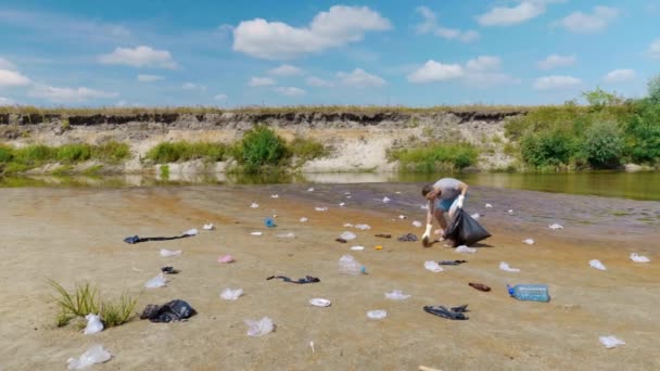 Människan dansar, sjunger och samlar plastskräp på stranden av förorenade floden — Stockvideo