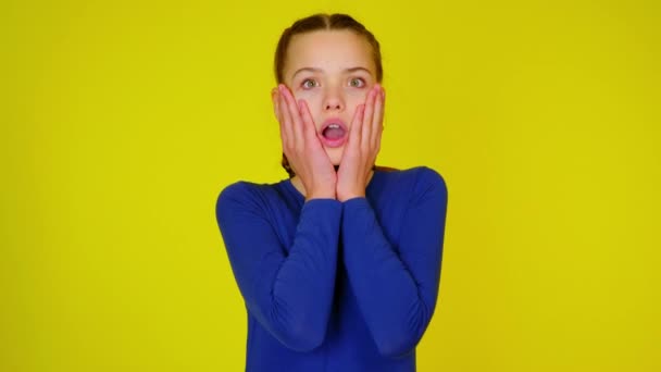 Tonåring flicka i blå pullover är sätter händerna mot huvudet, öppnar munnen och mycket förvånad — Stockvideo