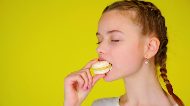 Teenage girl in a white T-shirt bites a white macaroon and enjoys its taste — Stock Video
