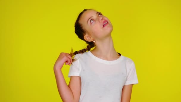 Teenage girl in a white T-shirt chews gum and twists a pigtail. — Stok video