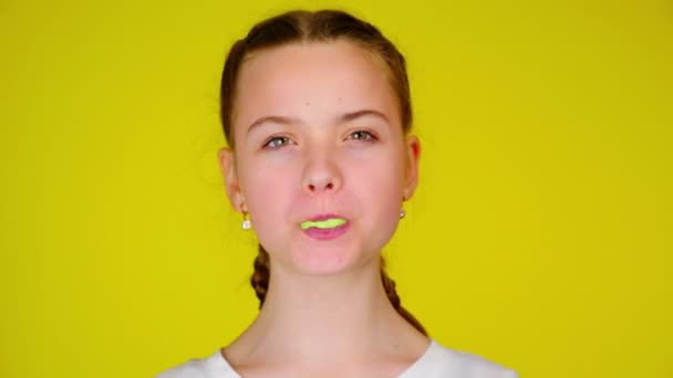 Teenage girl in a white T-shirt chews gum and inflates a bubble — Stock video