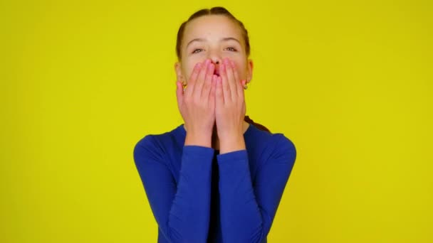 Teenage girl in blue pullover blows a kiss on yellow background — Stock Video
