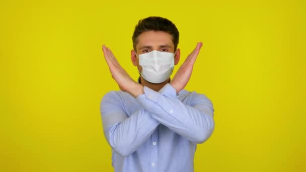 Young man in a medical mask looks at camera and keeps his arms crossed — Αρχείο Βίντεο