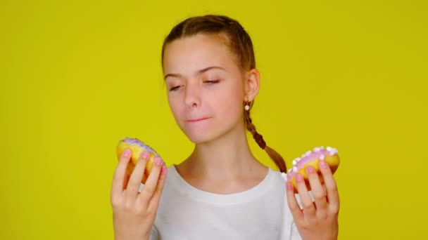 Tiener meisje in een wit T-shirt kijkt naar donuts en wil ze eten — Stockvideo