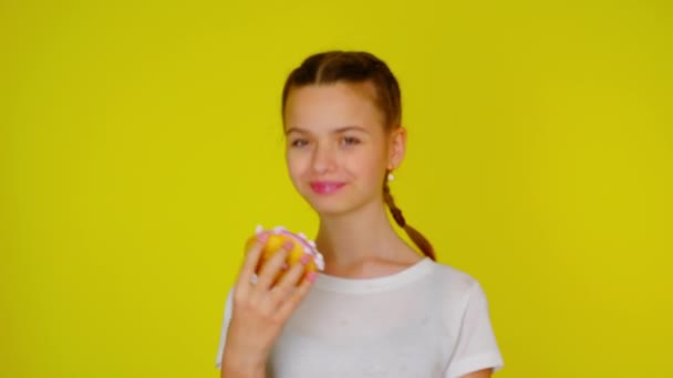 Teenage dívka v bílém tričku ukazuje růžový kobliha a úsměvy — Stock video
