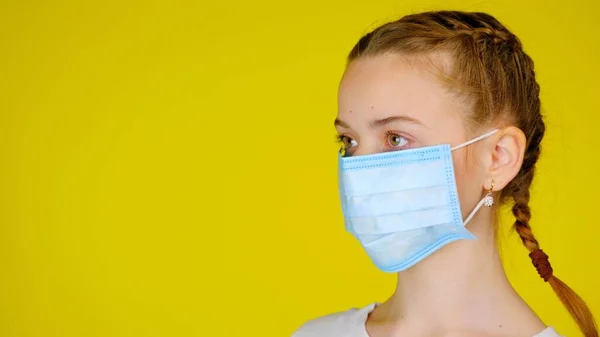 Tini lány orvosi maszk félprofilú néz félre a sárga háttér — Stock Fotó
