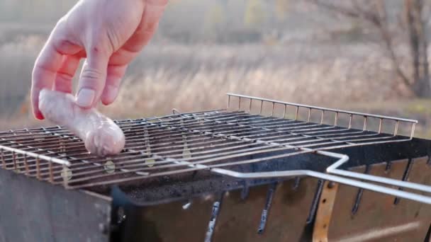 De mannelijke hand legt de worst op de grill. Begrip koken in de barbecue — Stockvideo