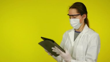 Tıp önlüklü genç kadın, koruyucu maske tablet kullanıyor.