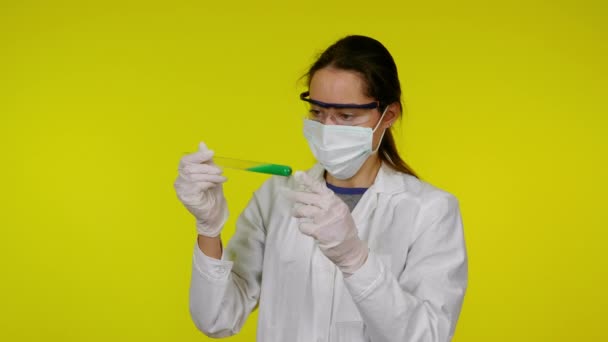 Mujer en bata médica blanca, máscara protectora se examina el contenido del tubo de ensayo — Vídeo de stock