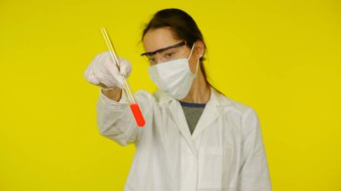 Tıbbi maskeli, gözlüklü ve lateks eldivenli doktor testlere matarayla bakar.