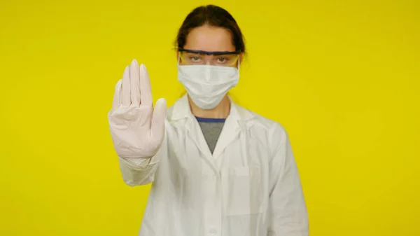Fiatal orvos orvosi maszkban, szemüveg és gumikesztyű mutatja a stop kézzel — Stock Fotó