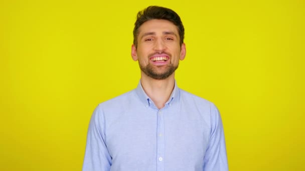 Young man in light blue shirt is laughs and looks at camera — Stockvideo