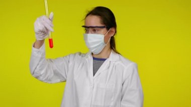 Koruyucu maskeli kadın test tüpünün içeriğini inceliyor ve hoşlanmadığını gösteriyor.