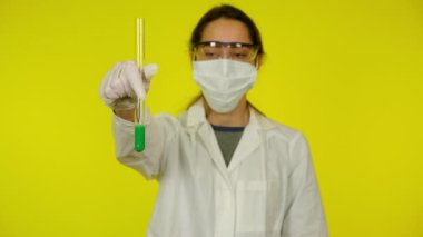 Beyaz elbiseli kadın, koruyucu maske test tüpünün içindekileri inceliyor.