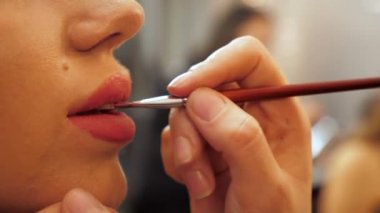 Profesyonel makyaj sanatçısı güzellik salonunda bir kadına dudak boyuyor.