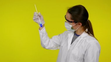 Beyaz elbiseli kadın, koruyucu maske test tüpünün içindekileri inceliyor.
