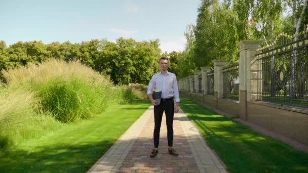Geschäftsmann steht mit Laptop in der Hand in einem Park und blickt in die Kamera — Stockvideo