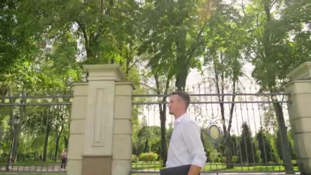 Biznesmen z laptopem w ręku spaceruje po parku — Wideo stockowe