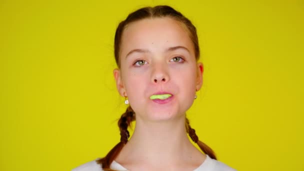 Teenage girl in a white T-shirt chews gum and inflates a bubble — Stock video