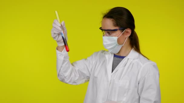 Vrouw in witte medische jurk, beschermend masker is onderzoekt de inhoud van de reageerbuis — Stockvideo