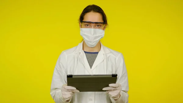 Orvos tablettával a kezében, védőorvosi maszk, szemüveg és latex kesztyű — Stock Fotó