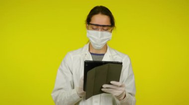 Tıp önlüklü genç kadın, koruyucu maske tablet kullanıyor.