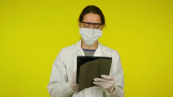 Young woman in medical coat, protective mask is uses tablet — Stock Video