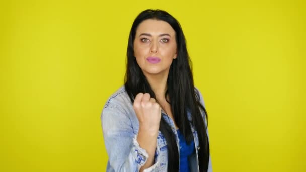 Kvinna visar en knytnäve mot kameran på en gul bakgrund med kopieringsutrymme — Stockvideo